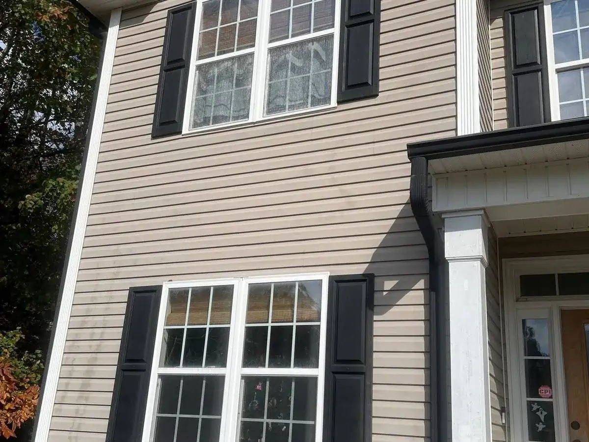 Tan vinyl siding with dark vertical streaks left by a high pressure tip