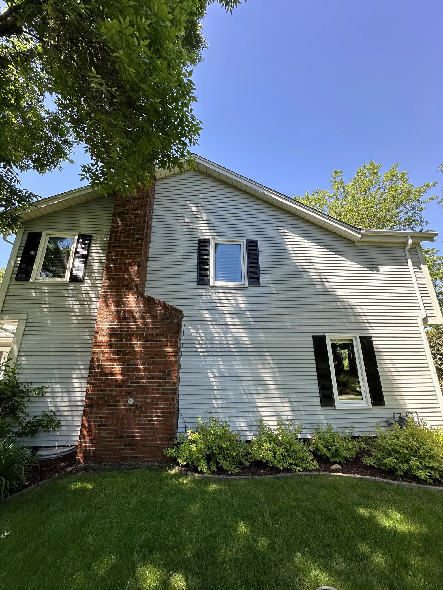 Gable end and brick chimney of a Brookfield home before washing, growth across the siding