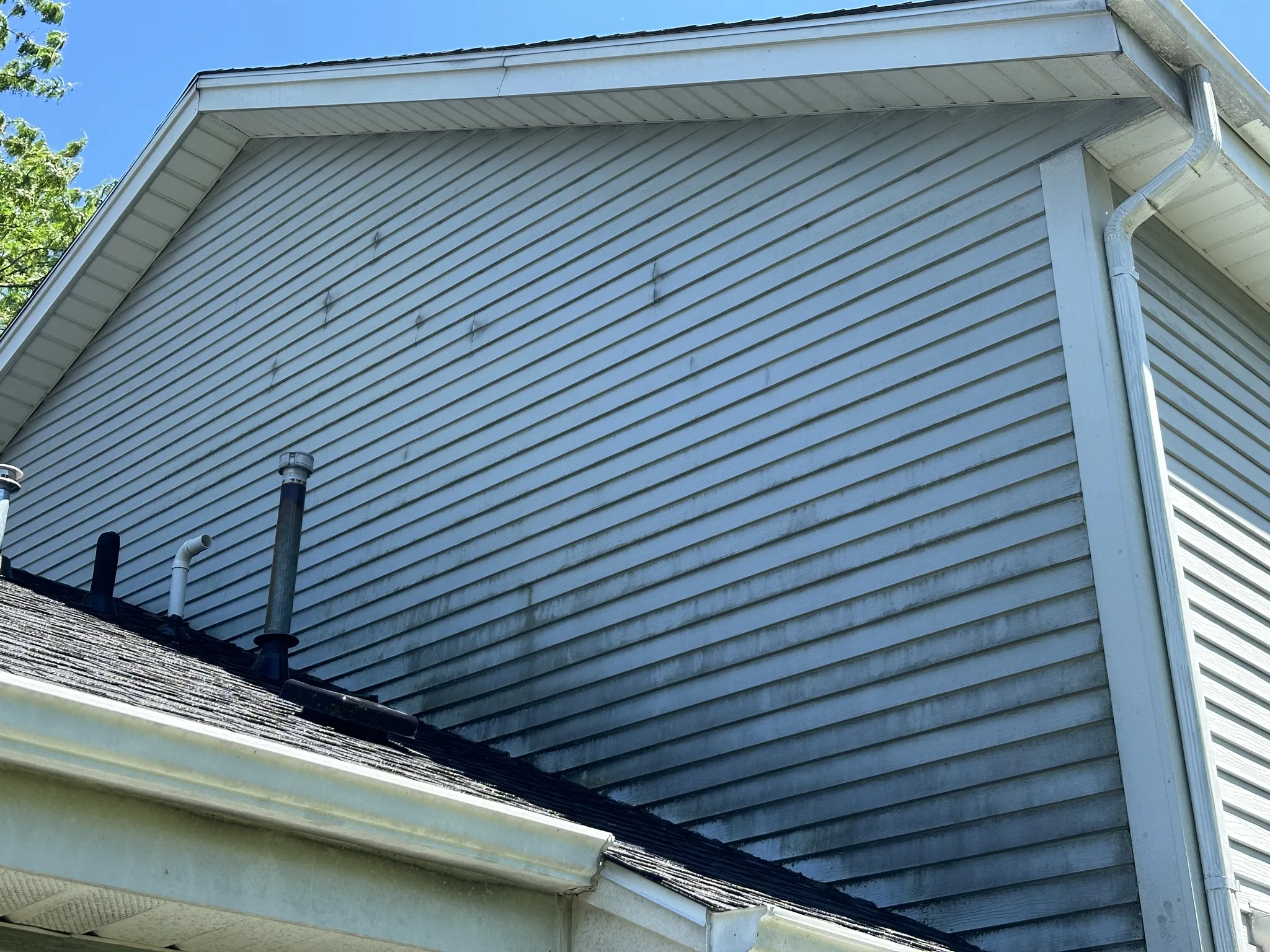 Upper gable of a Brookfield home before soft washing, siding darkened with organic growth and staining along the roof line
